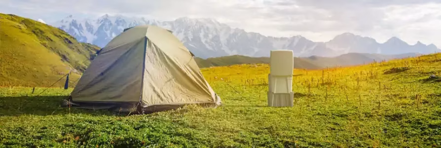 Camping Toilet Solutions: Your Guide to Comfortable Outdoor Hygiene Camping tent and portable toilet set up on a grassy field with mountains in the background under a partly cloudy sky