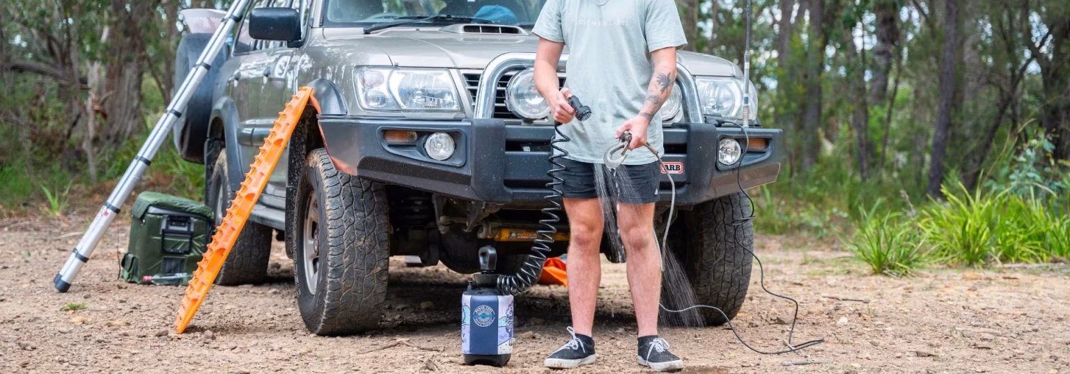 How to Choose the Best Portable Camping Shower Man using portable outdoor shower next to off-road SUV with roof tent setup in forest campsite