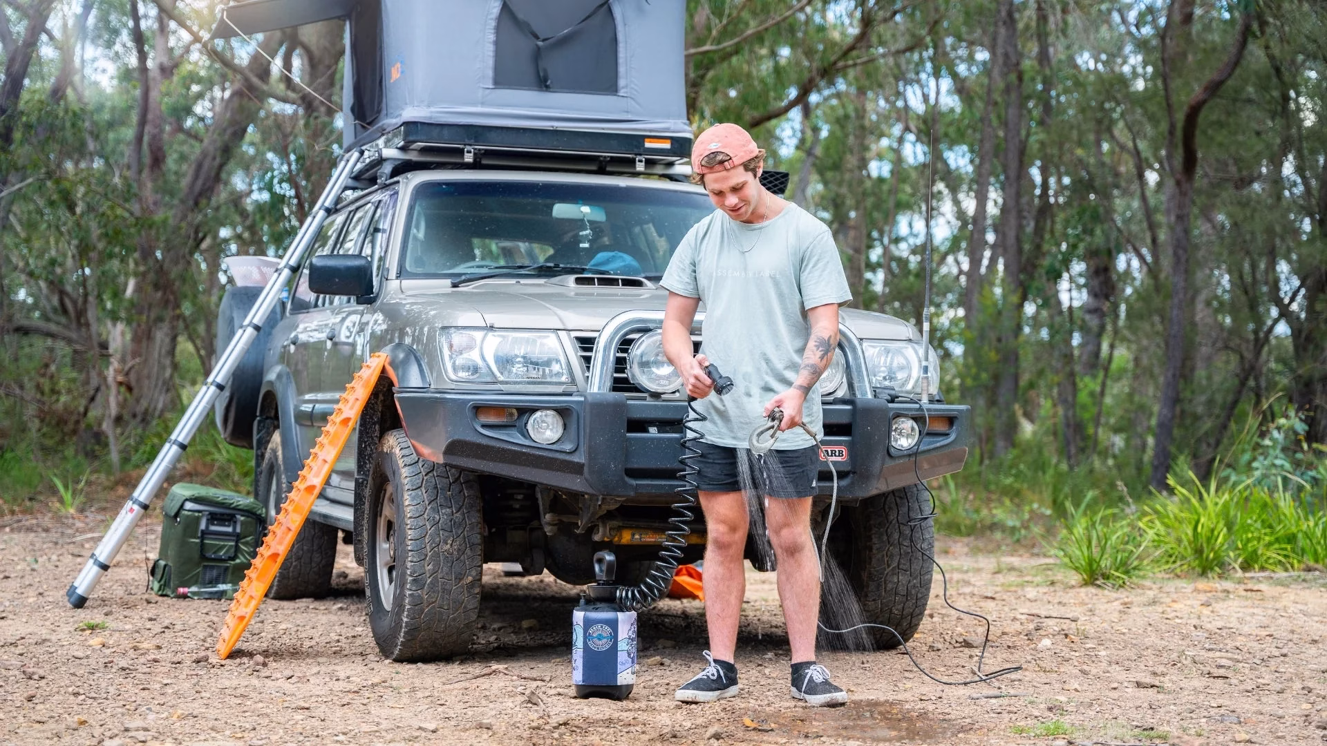 How to Choose the Best Portable Camping Shower 2 Man using portable outdoor shower next to off-road SUV with roof tent setup in forest campsite
