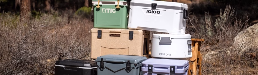 A variety of camping coolers in different sizes and colors displayed on a picnic table outdoors.