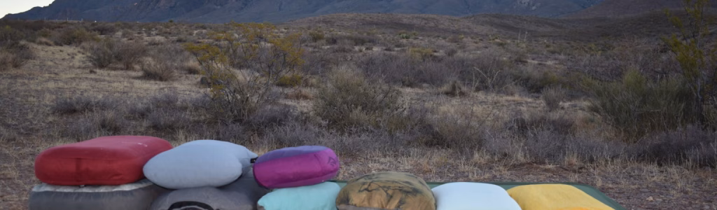 the Perfect Camping Pillow Comfort: Unlock Unrivaled Comfort A variety of camping pillows arranged on a sleeping pad in a desert landscape at sunset, with rugged mountains in the background — showcasing different sizes, shapes, and compressibility of travel pillows for outdoor sleep comfort.