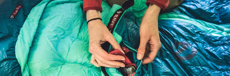 Person storing small items inside the inner pocket of a turquoise RAVE sleeping bag, ideal for organizing personal essentials during camping or outdoor adventures